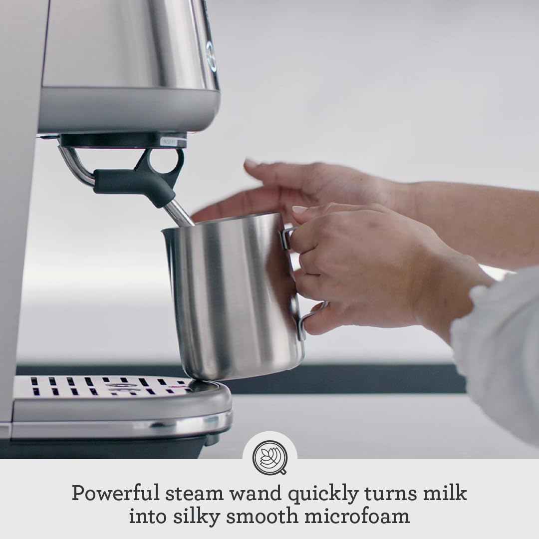 Steaming milk by hand using the Breville Bambino manual steam wand, with hands holding a stainless steel milk pitcher under the wand